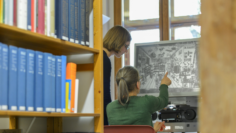 Eine Person zeigt einer anderen im Lesesaal der Bibliothek ein Bild am Rechner
