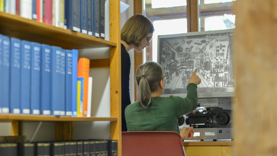 Eine Person zeigt einer anderen im Lesesaal der Bibliothek ein Bild am Rechner