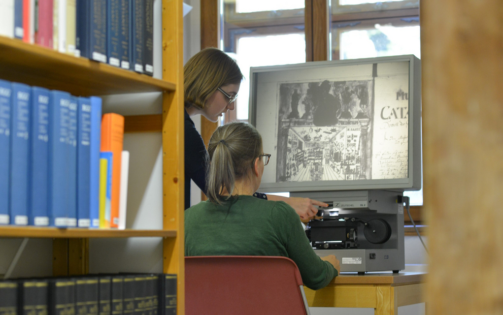 Zwei Frauen in einer Bibliothek betrachten an einem Lesegerät ein alte Abbildung