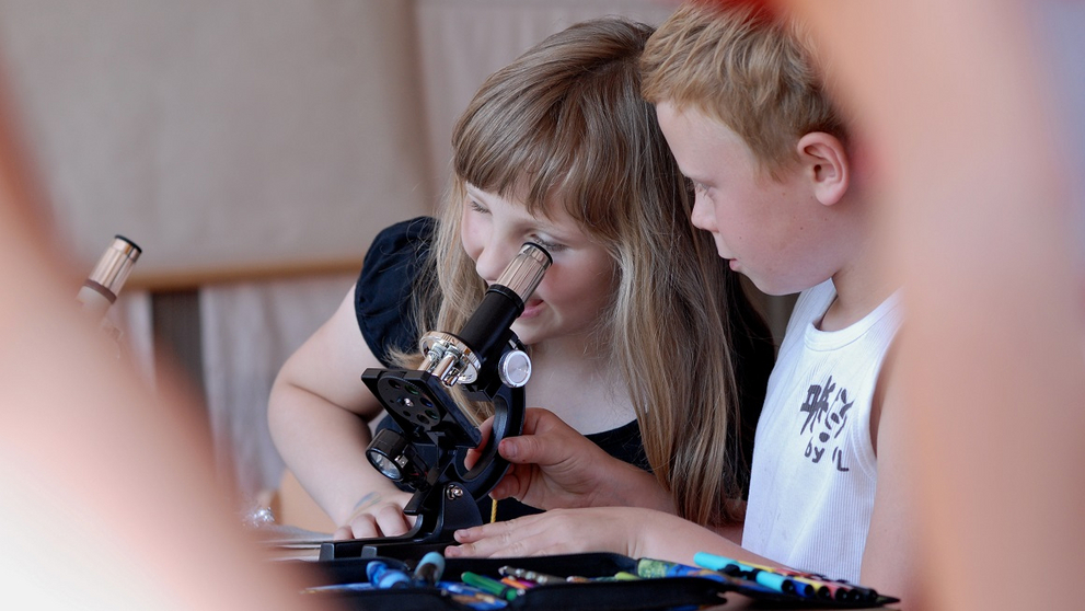 Ein Junge und ein Mädchen experimentieren mit einem Mikroskop.