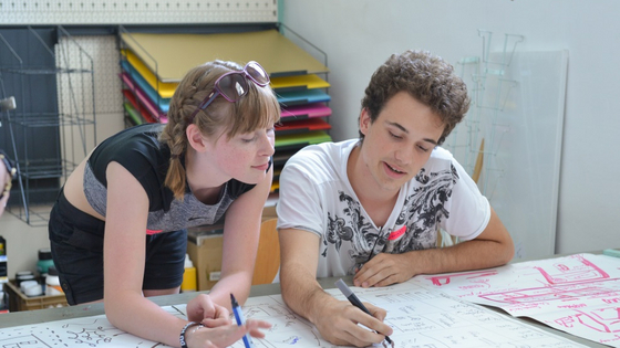 Eine Junge und ein Mädchen beugen sich über ein großes Blatt Papier und planen ein gemeinsames Projekt.