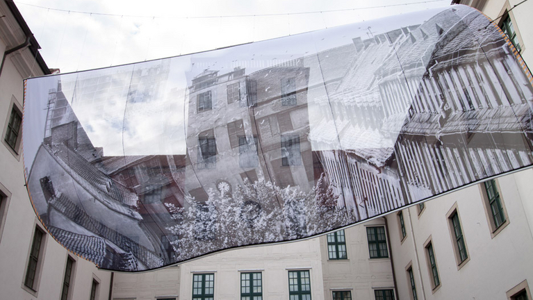 An der Rückseite von Haus 1 hängt quer über den Lindenhof ein Riesenbanner mit einem Foto von 1990.