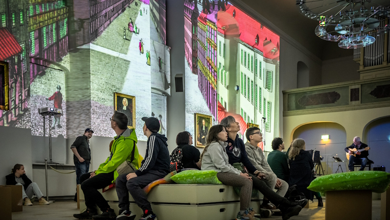 Gäste der Museumsnacht sitzen im Freylinghausen-Saal inmitten des raumgroß an die Wand projizierten Stichs des Lindenhofs aus dem 18. Jahrhundert.