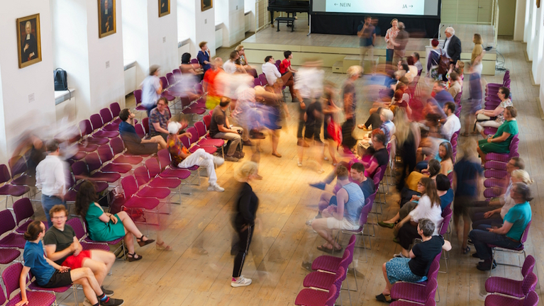 Der Freylinghausen-Saal mit Besucher:innen der Unterhausdebatte von oben