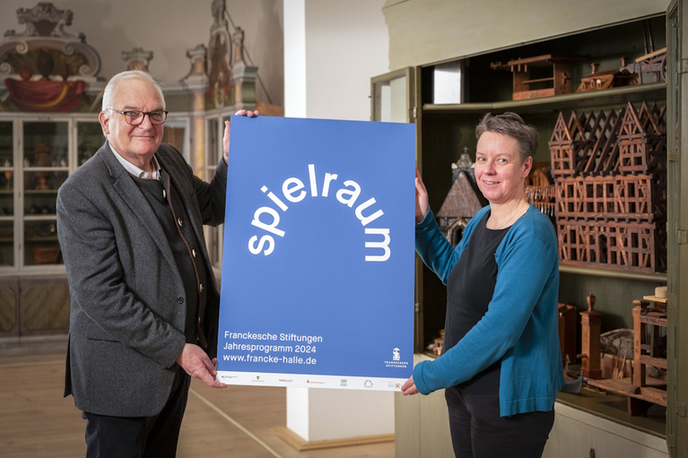 Foundation Director Müller-Bahlke and Deputy Director von Biela show the poster for the annual "Spielraum" programme in front of the open model cabinet in the Cabinet of Artfects and Natural Curiosities.