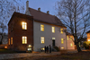 The light is on in the small house, and people are standing in front of it.