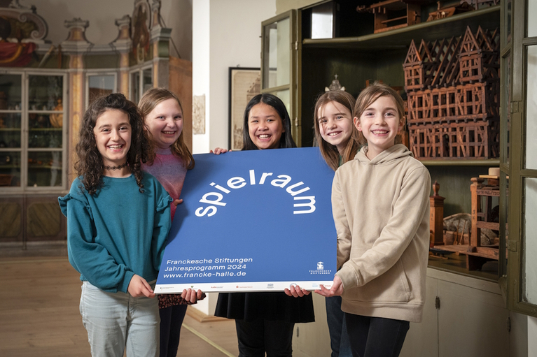 Five girls from the August Hermann Francke nursery show the poster for the annual exhibition in the Kunst- und Naturalienkammer in front of the historical school model collection.