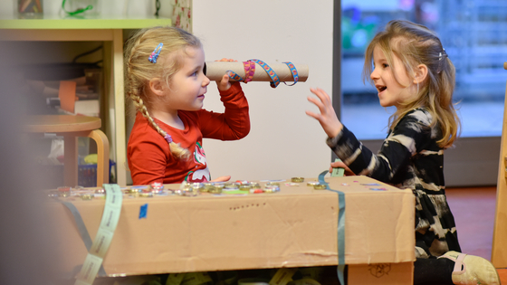 Zwei Kinder spielen mit einem Rohr aus Pappkarton