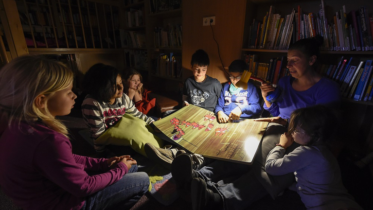 Kinder lesen in der gemütlich-dunklen Bibliothek mit der Taschenlampe gemeinsam ein Buch. 