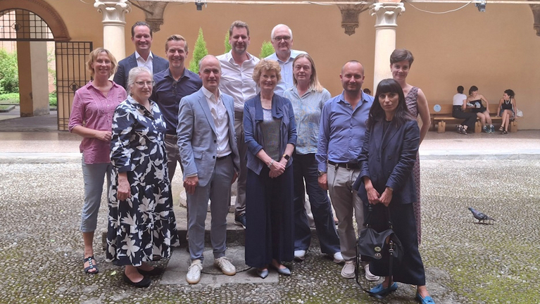 Participants of the Workshops of the Alliance of Early Universal Museums are gathered for a group photo in a historic courtyard in Bologna.