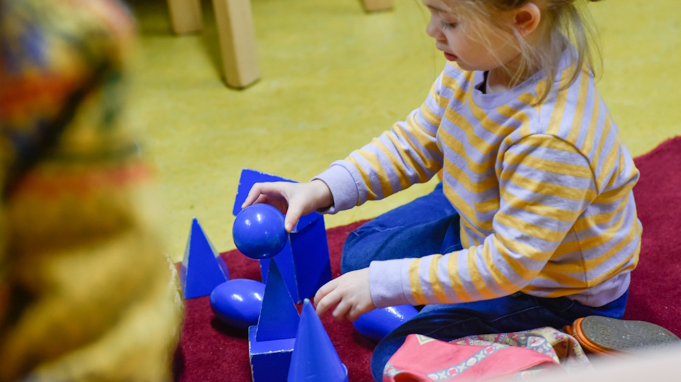 A girl is playing on the floor with blue balls, skittles and wooden blocks.