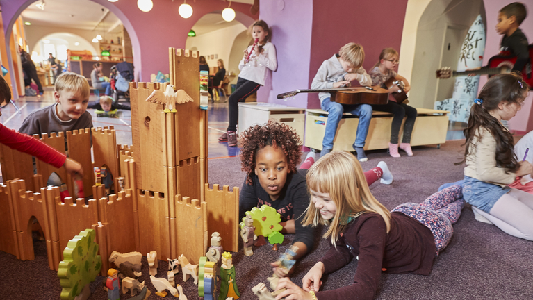 Kinder im Krokoseum bauen ein Schloss aus Holzteilen, spielen Instrumente oder mit Puppen. 