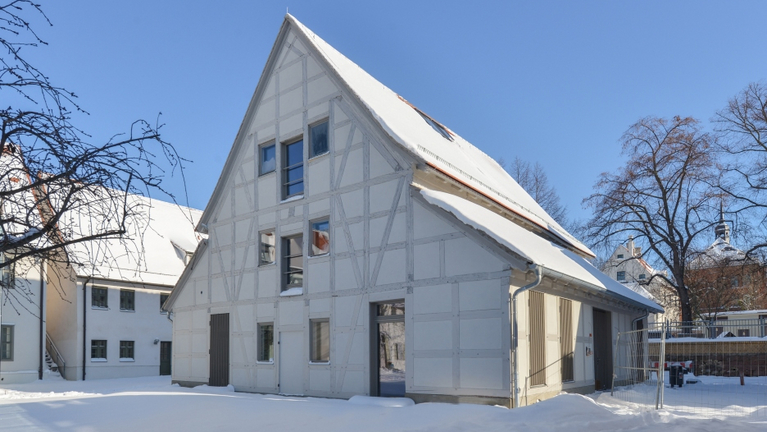 Ansicht des strahlend weißen, frisch sanierten Gebäudes der Kleinen Scheune vor blauem Himmel und im Schnee.